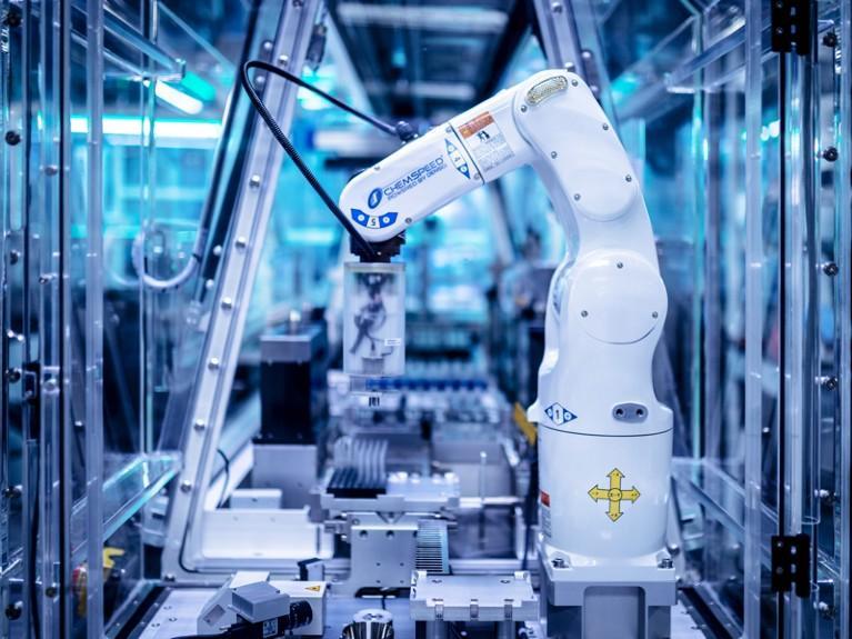 A robotic arm inside an enclosed, automated laboratory handling sample racks — the kind of remotely operated 'cloud lab' system that executes experiments without a human ever entering the room.