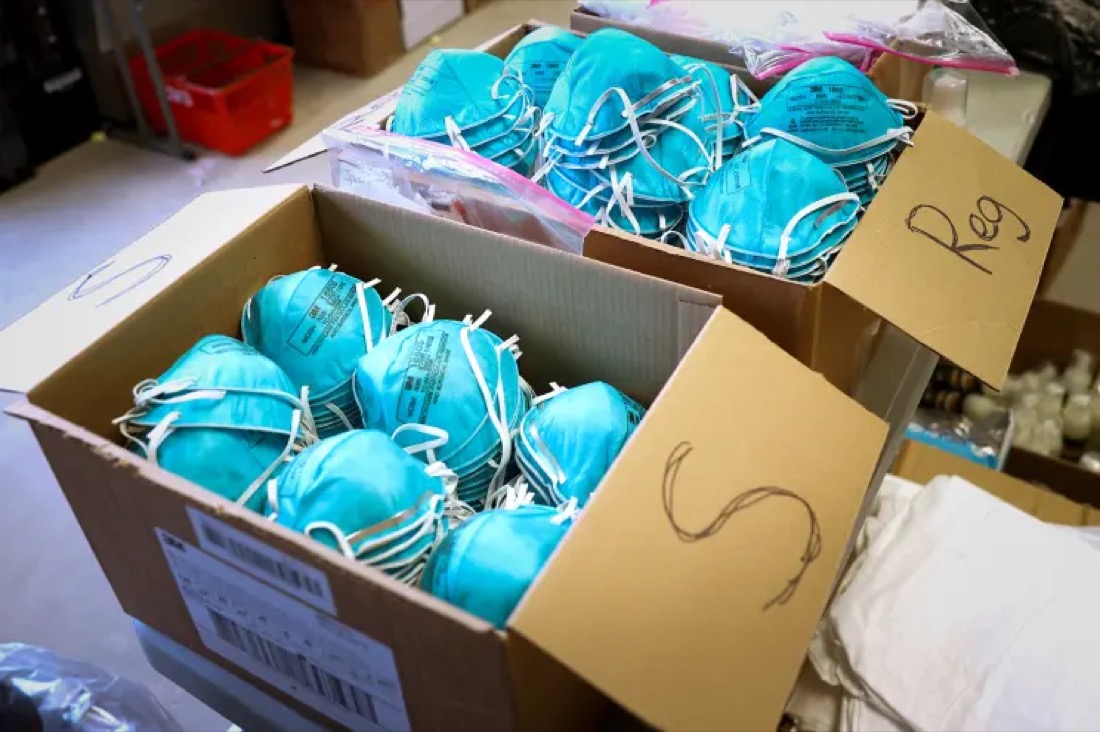 Open cardboard boxes filled with blue N95-style respirator masks.